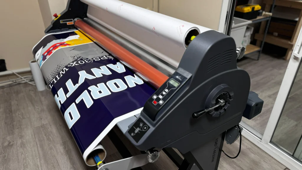 A large printer positioned on a table beside a sizable sheet of paper, illustrating digital printing services in action.